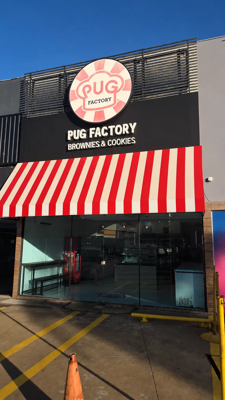 Fachada da matriz PUG Factory em Maringá, com letreiro da marca e toldo listrado vermelho e branco